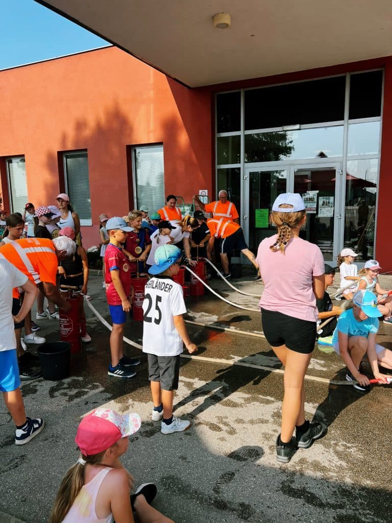 Feuerwehr Zettling beim Schulsportfest der Volksschule Premstätten 2025 – Kübelspritzen-Station mit Erinnerungsbuttons und Jugendfolder für die Kinder