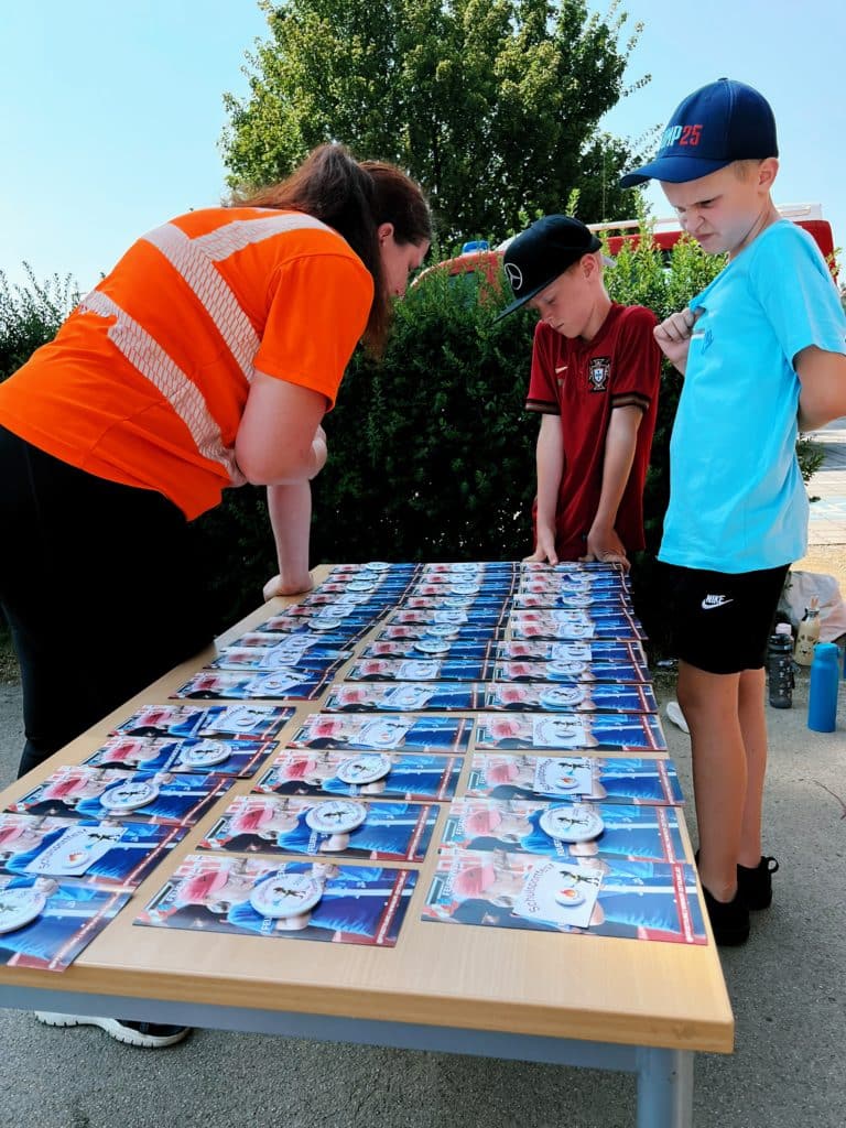Feuerwehr Zettling beim Schulsportfest der Volksschule Premstätten 2025 – Kübelspritzen-Station mit Erinnerungsbuttons und Jugendfolder für die Kinder