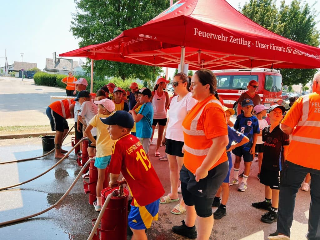 Feuerwehr Zettling beim Schulsportfest der Volksschule Premstätten 2025 – Kübelspritzen-Station mit Erinnerungsbuttons und Jugendfolder für die Kinder