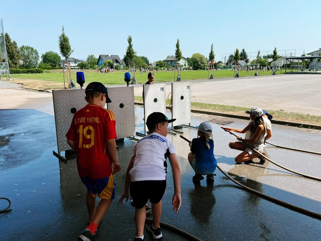 Feuerwehr Zettling beim Schulsportfest der Volksschule Premstätten 2025 – Kübelspritzen-Station mit Erinnerungsbuttons und Jugendfolder für die Kinder