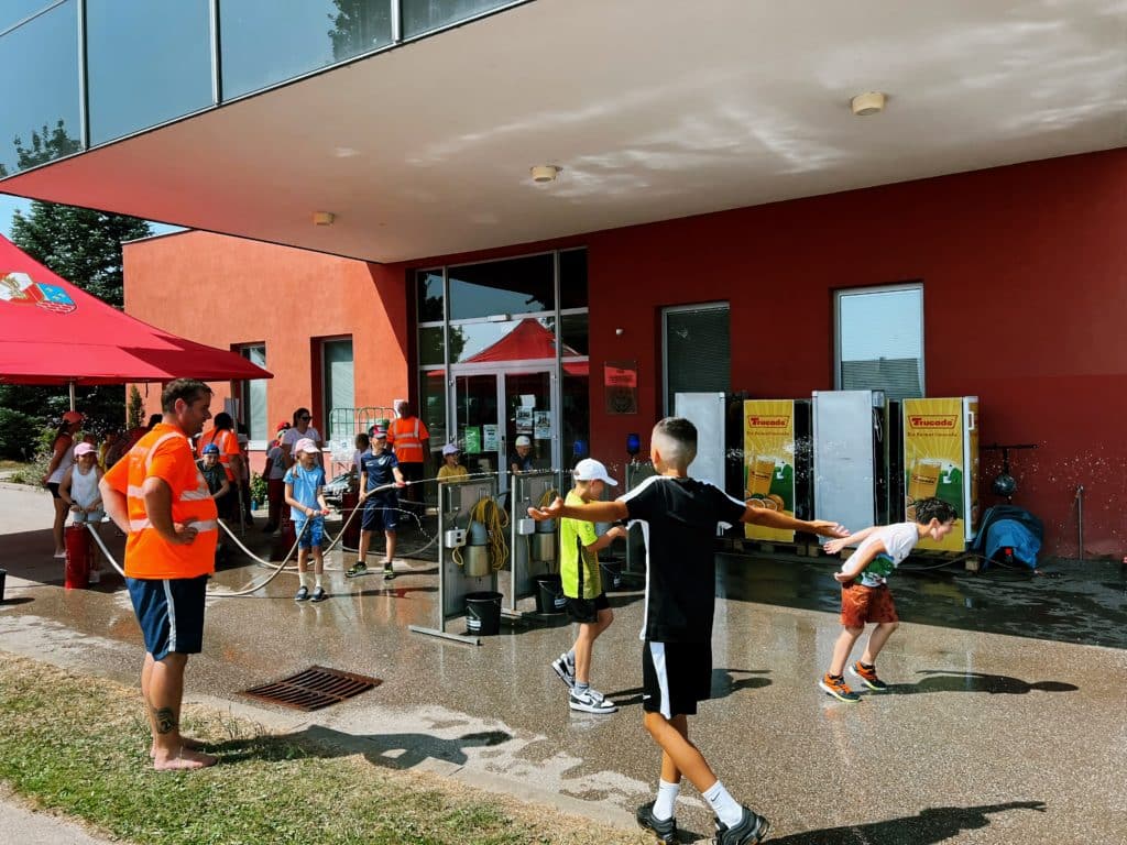 Feuerwehr Zettling beim Schulsportfest der Volksschule Premstätten 2025 – Kübelspritzen-Station mit Erinnerungsbuttons und Jugendfolder für die Kinder
